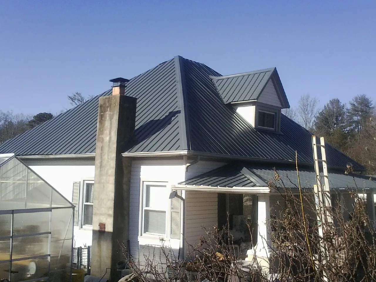 Dark blue standing seam metal roof on a white farmhouse with dormer — Slate & Tile Roof Repair by Roofing Brothers in Dows