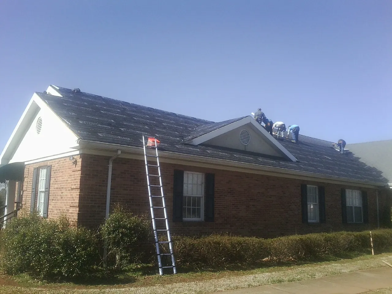 Crew tearing shingles off a brick ranch roof with a ladder set — Emergency Roof Repair work by our crew in Dows