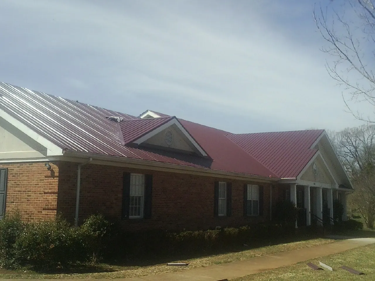 Red metal roof with gabled entries on a long brick building, from a Hail Damage Roof Repair job in Dows