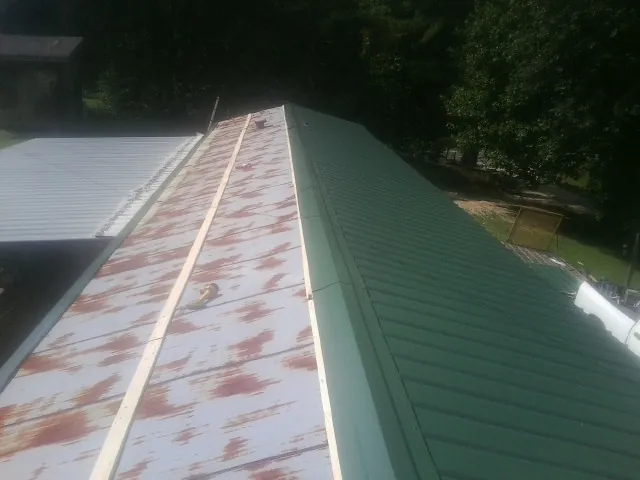 Old rusted panels beside newly installed green metal roofing — Wind Damage Roof Repair by Roofing Brothers in Dows