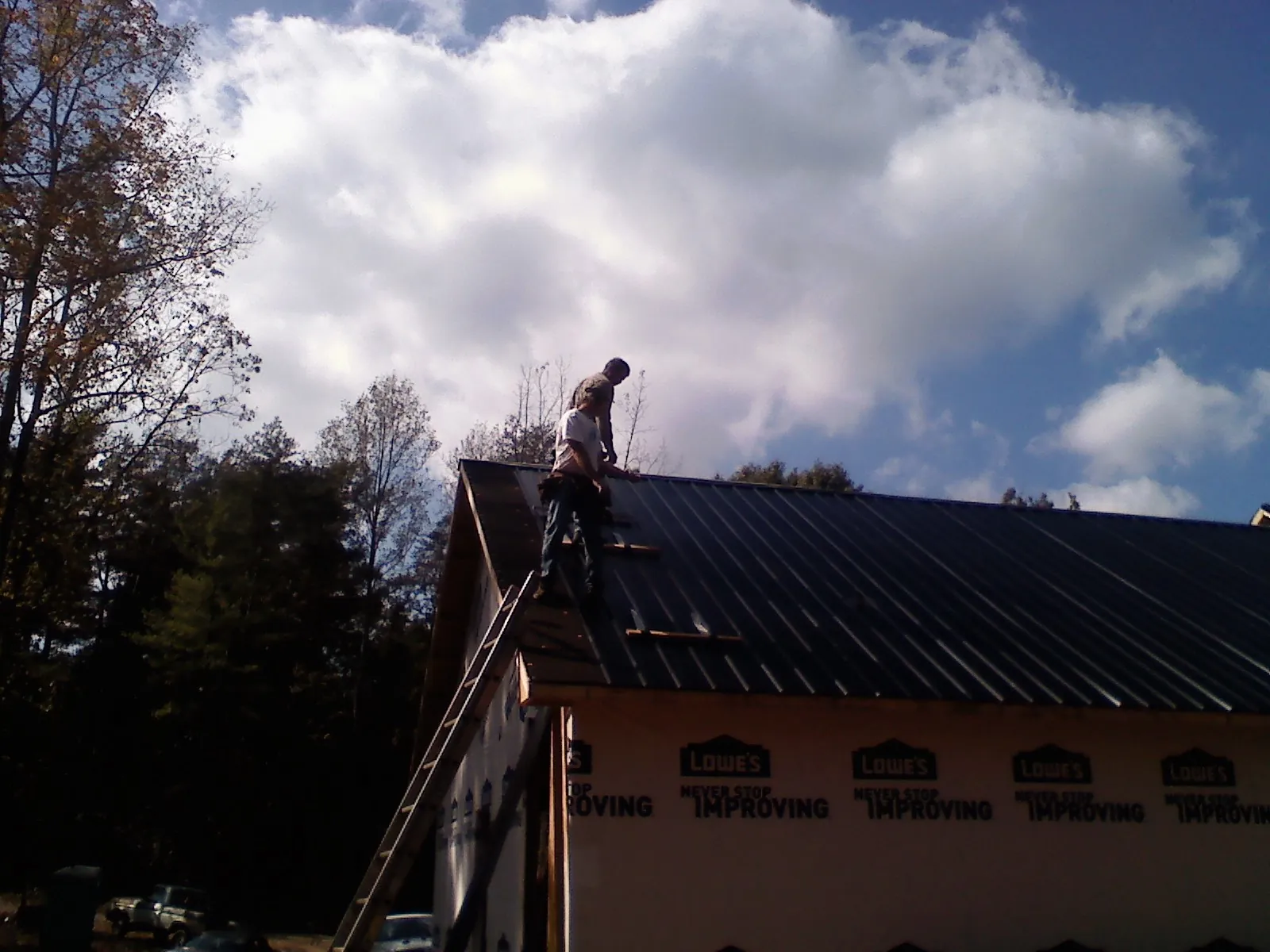 Roofer fastening dark metal panels high against a cloudy sky, from a Roof Inspection job in Dows