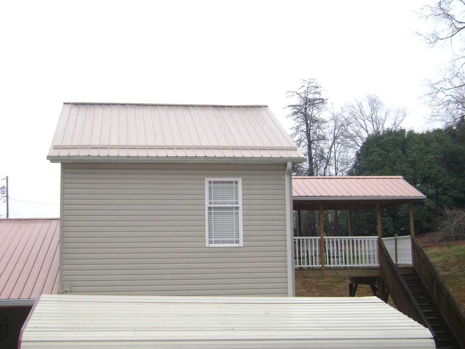 Tan metal roofs on a two story addition and attached porch, from a Roof Replacement job in Dows